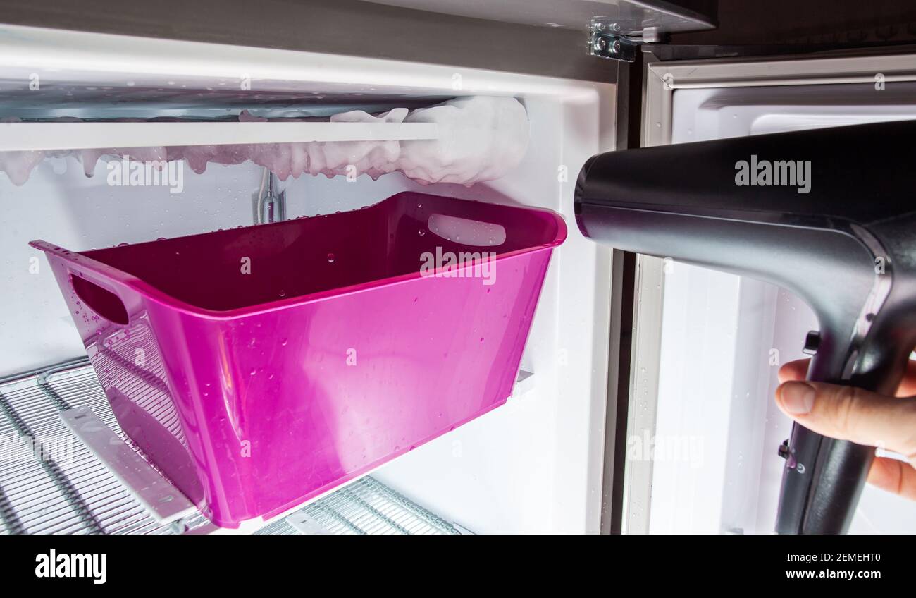 Process of defrosting ice in a home freezer. Collecting water in a plastic basin. Stock Photo