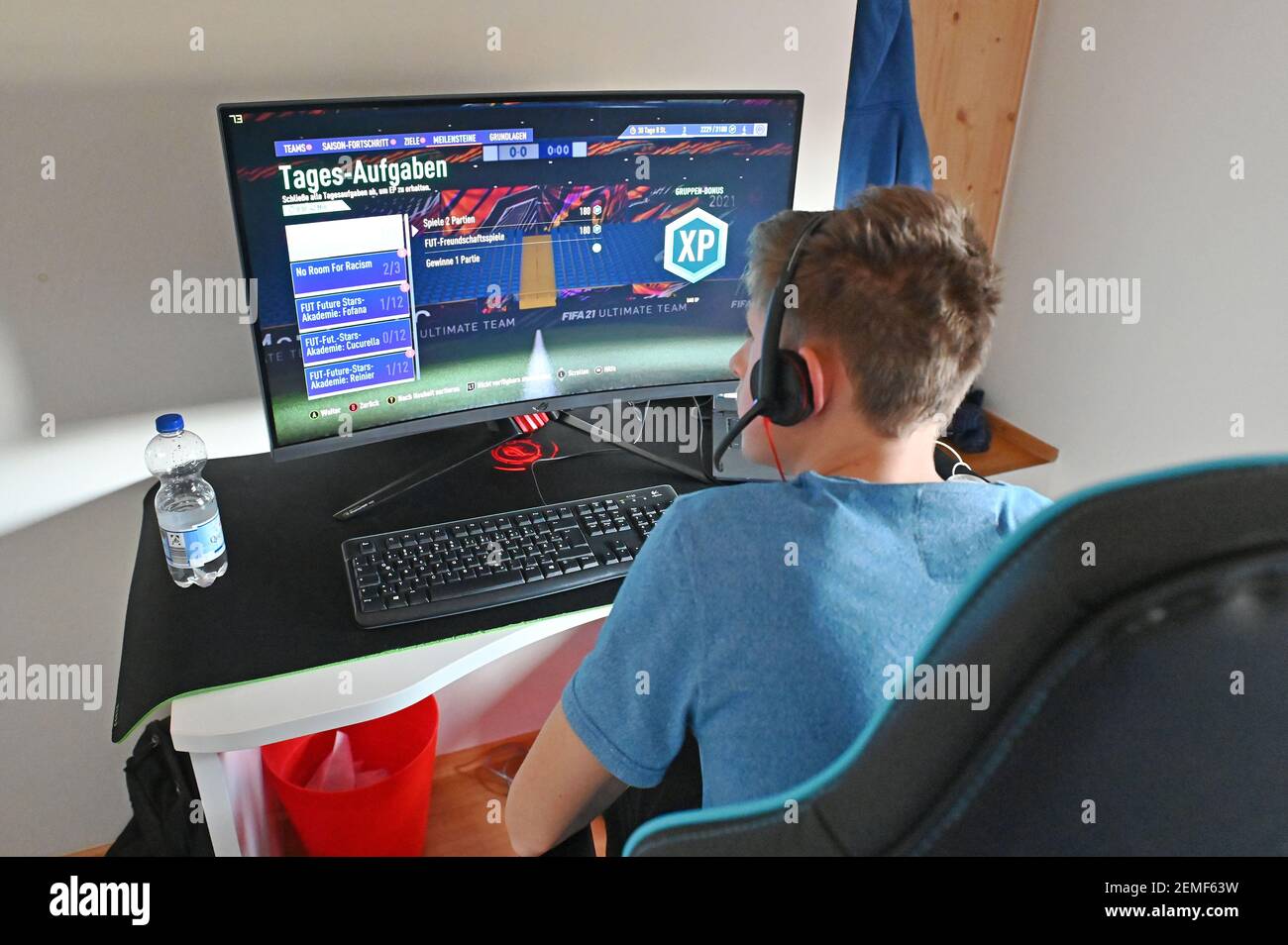 Munich, Deutschland. 24th Feb, 2021. Boy (14 years) plays the computer game  Fifa21 on his gaming PC. Sits in front of the monitor and wears a headset.  | usage worldwide Credit: dpa/Alamy