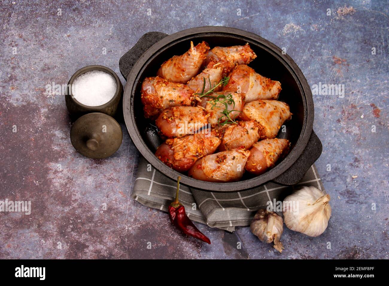 Marinated raw chicken legs on black pan. Uncooked marinated chicken