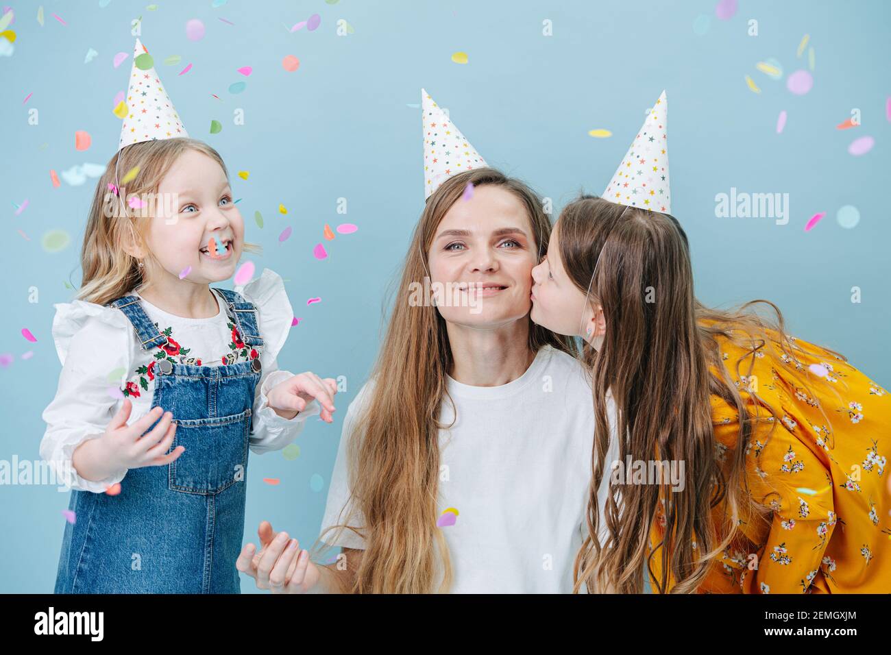 Daughters hugging their mother, all in party cones over blue Stock Photo