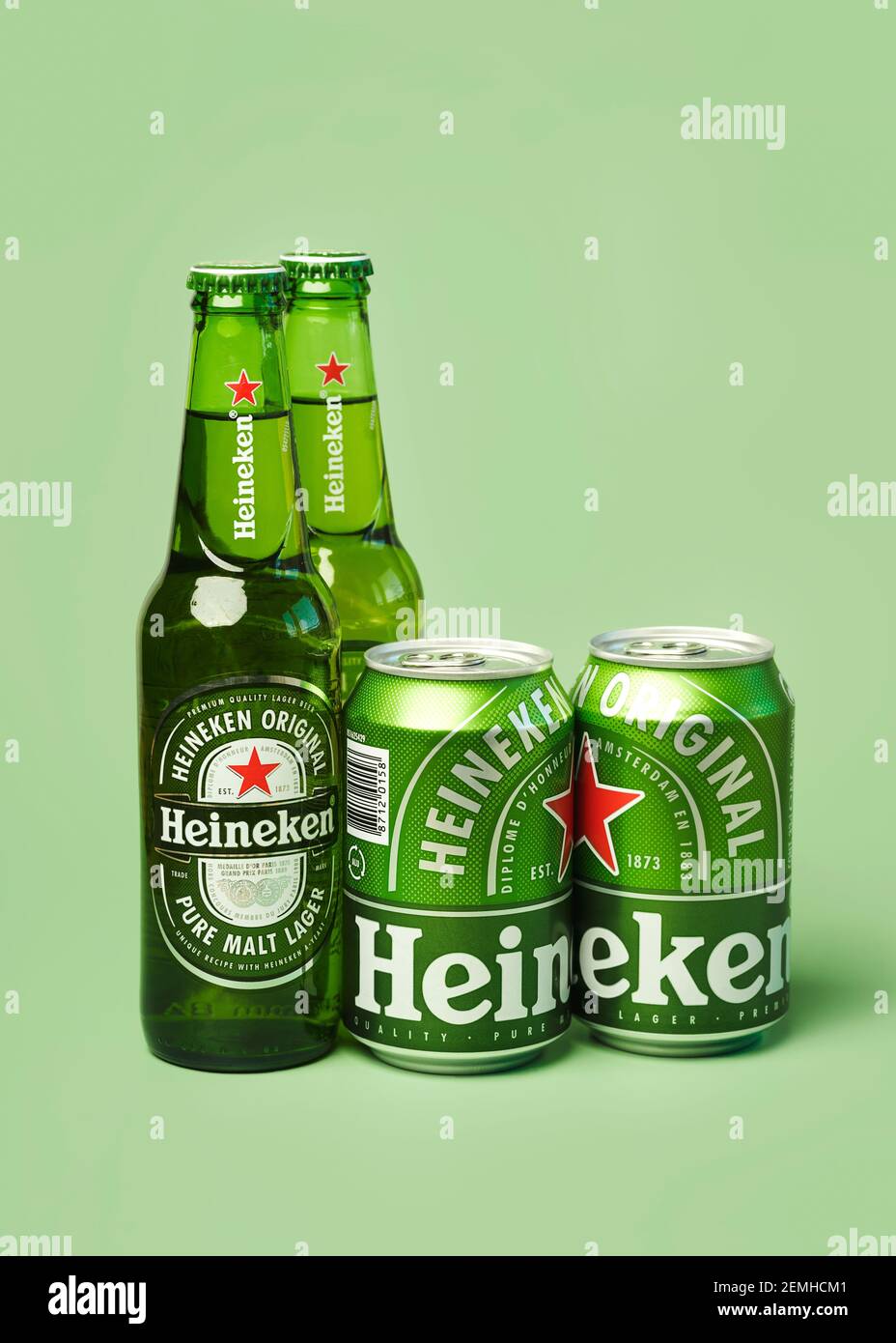 Heineken lager beer bottles and Heineken beer aluminum cans on green background Stock Photo