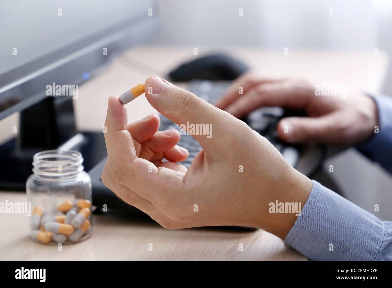Medication in capsule in male hands on PC keyboard background. Man taking pill during work at office Stock Photo