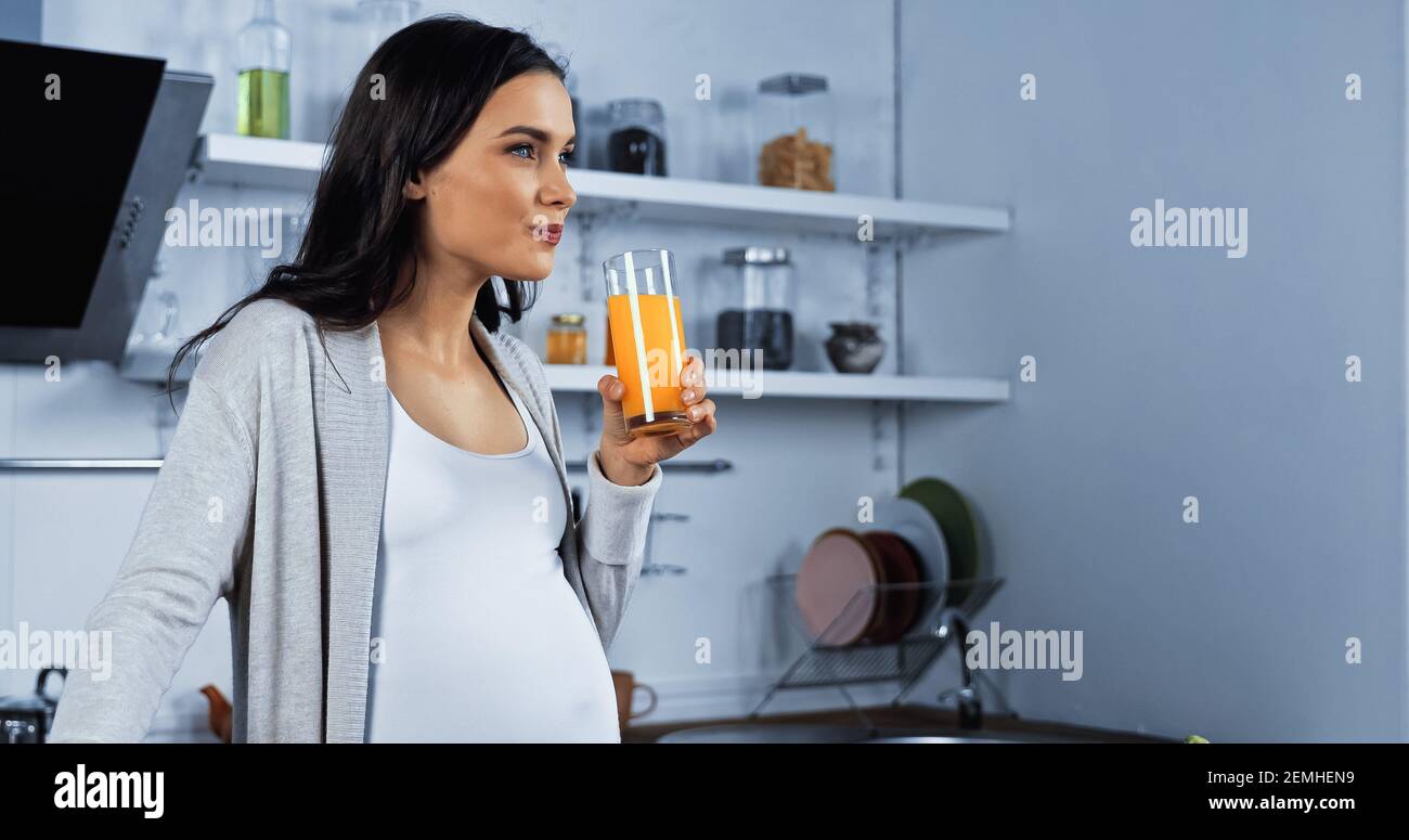 Pregnant brunette woman holding glass of orange juice in kitchen Stock ...