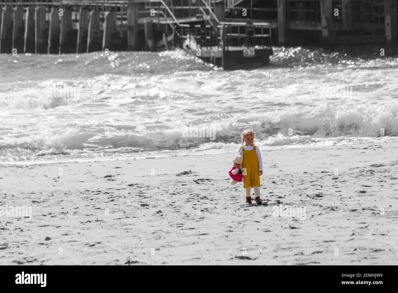 young girl holding teddy bear toy standing on the seashore at the seaside at Bournemouth beach, Bournemouth, Dorset UK in September - colour popping Stock Photo
