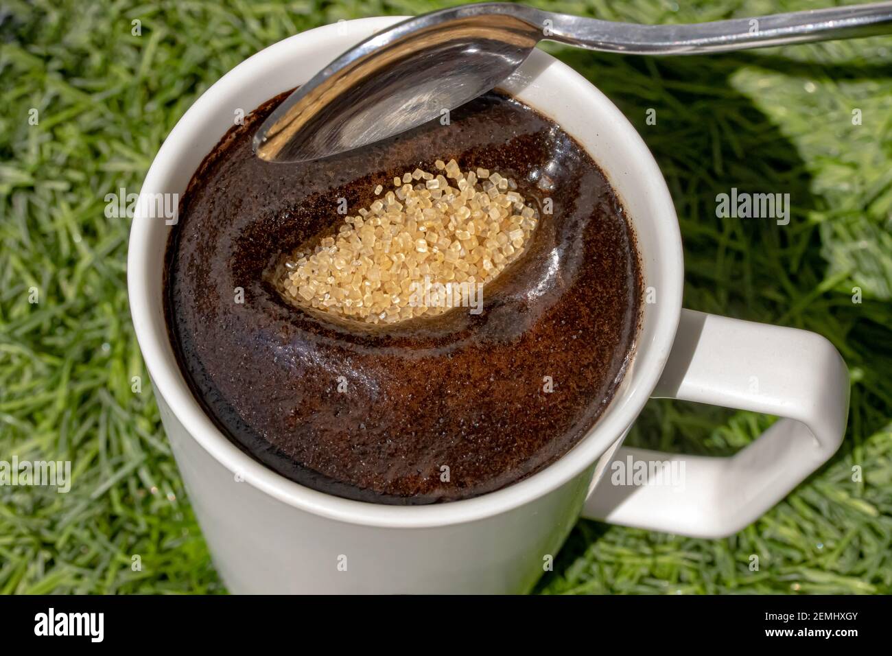 A teaspoon is pouring brown sugar into a cup of coffee, close up view