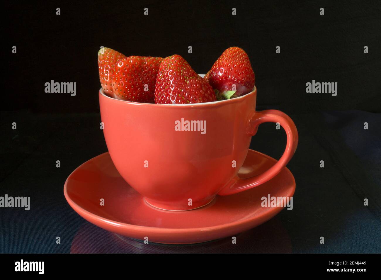 The Strawberries in cup on black background and table with reflection. Red ripe berries by summer Stock Photo