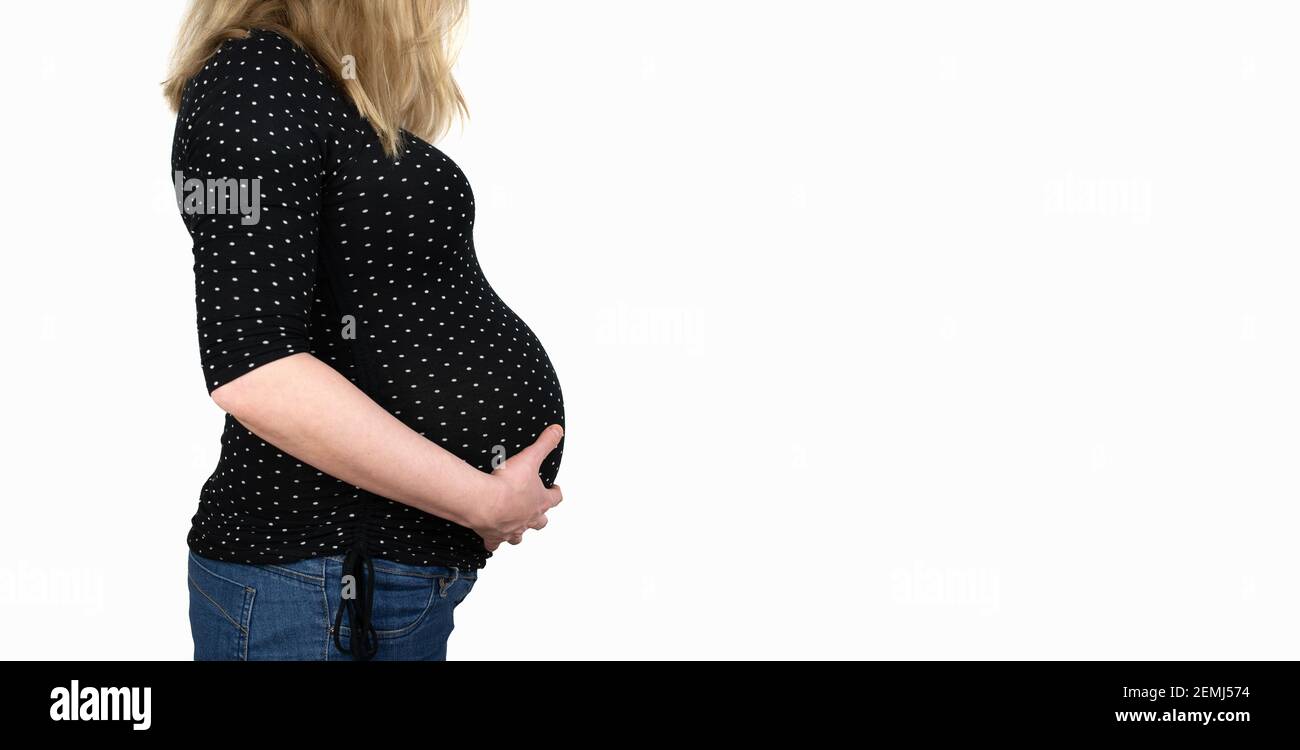 side view of midsection of 9 months pregnant woman in polka dotted shirt an jeans with hands on belly against white background Stock Photo