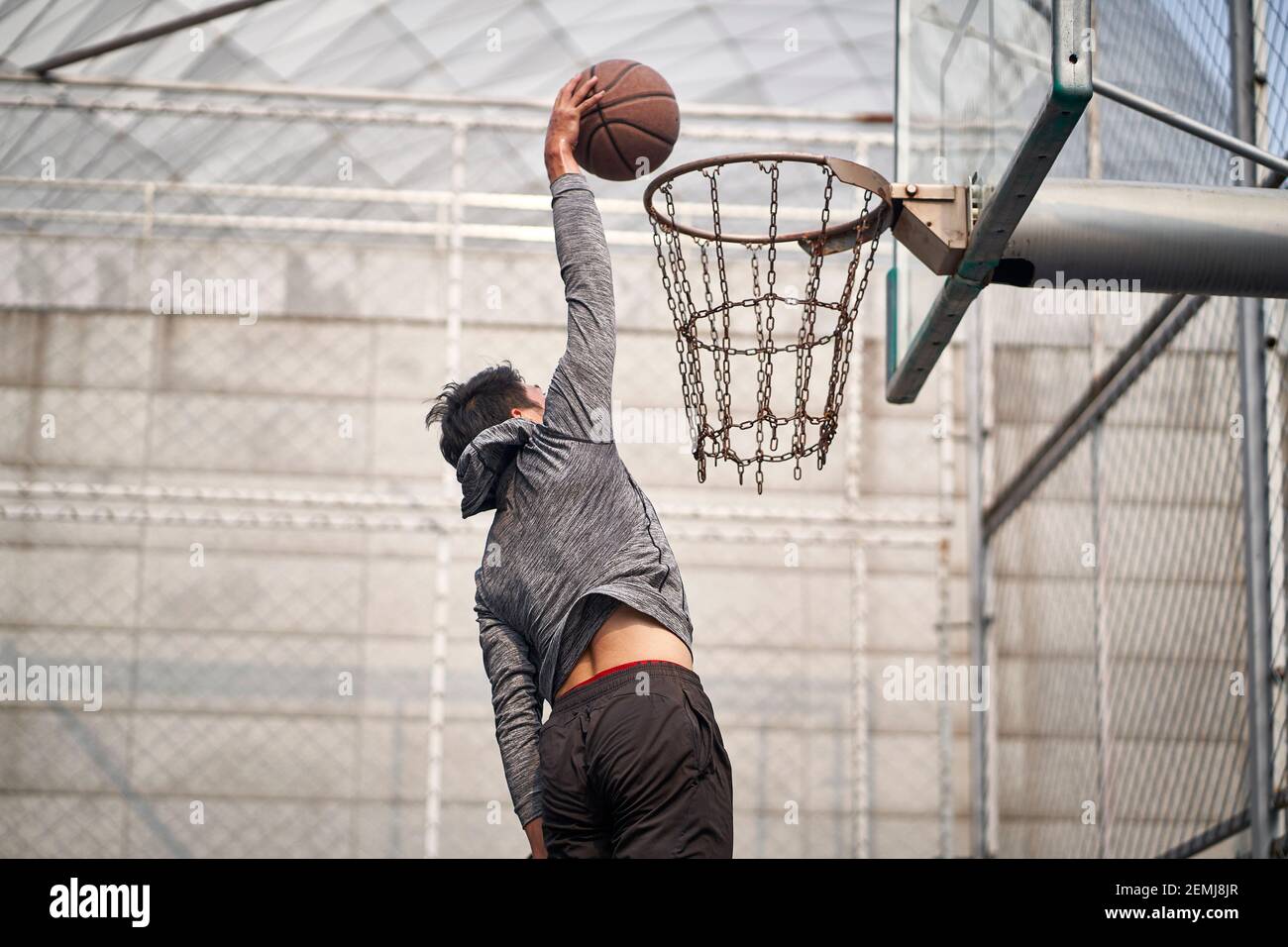 young asian adult man basketball player attempting a dunk on outdoor court Stock Photo