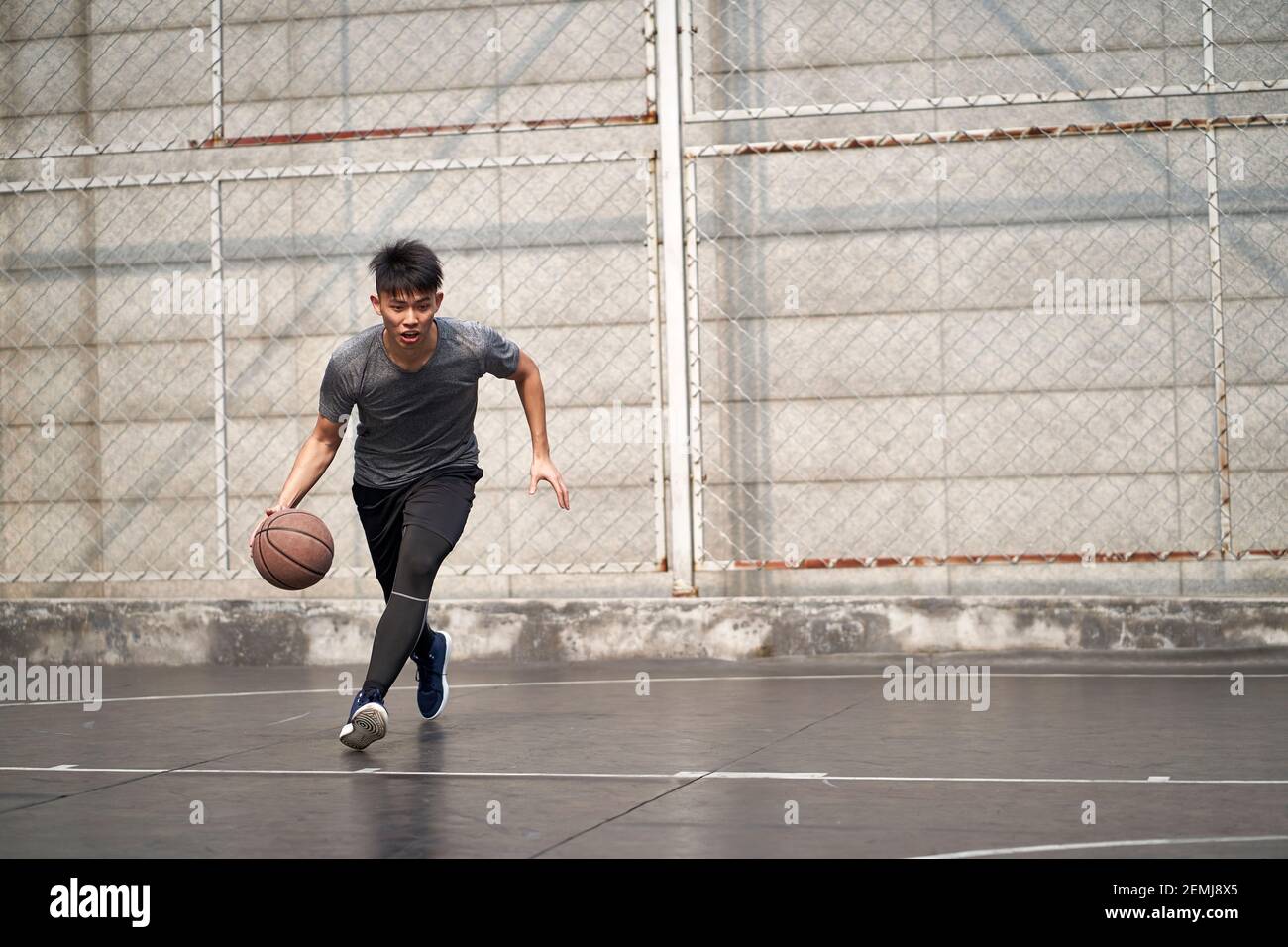 young asian man basketball player attempting a dunk on outdoor court Stock Photo