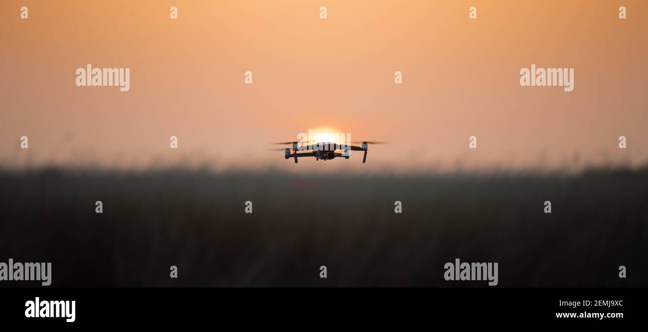 Drone quadcopter with digital camera in flight at sunset, Silhouette of drone at sunset Stock Photo