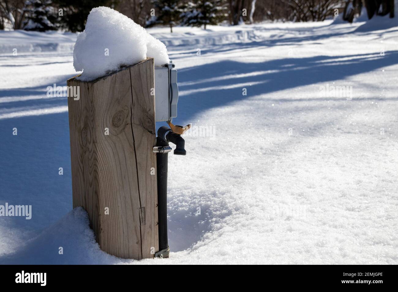 A water and electric hookup covered by snow during winter season on a closed campsite; water pump foutain Stock Photo