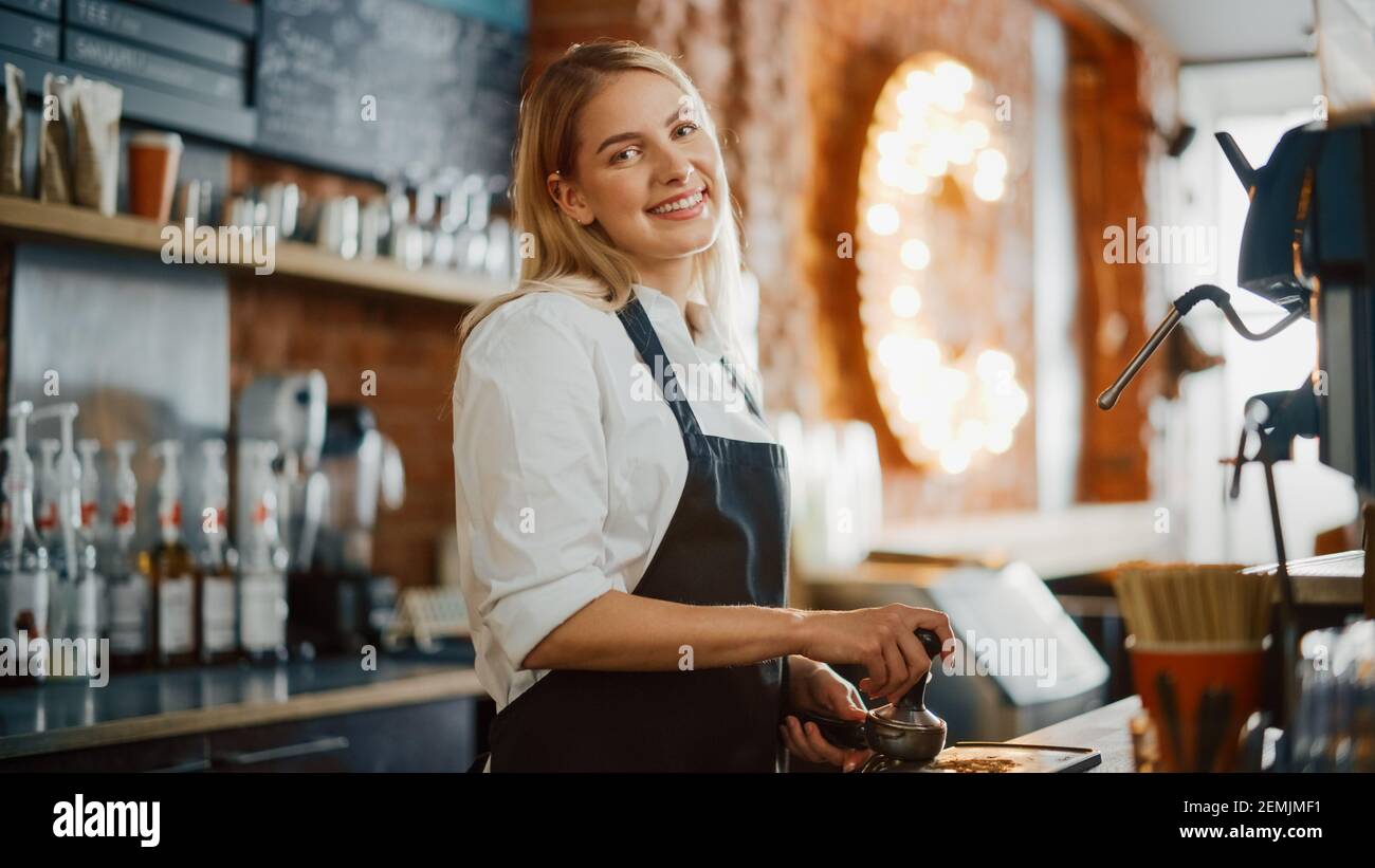 Beautiful Young Caucasian Barista with Blond Hair is Making a Cup of Fresh Coffee in a Cafe. Happy and Smiling Bar Employee Posing while Working in a Stock Photo