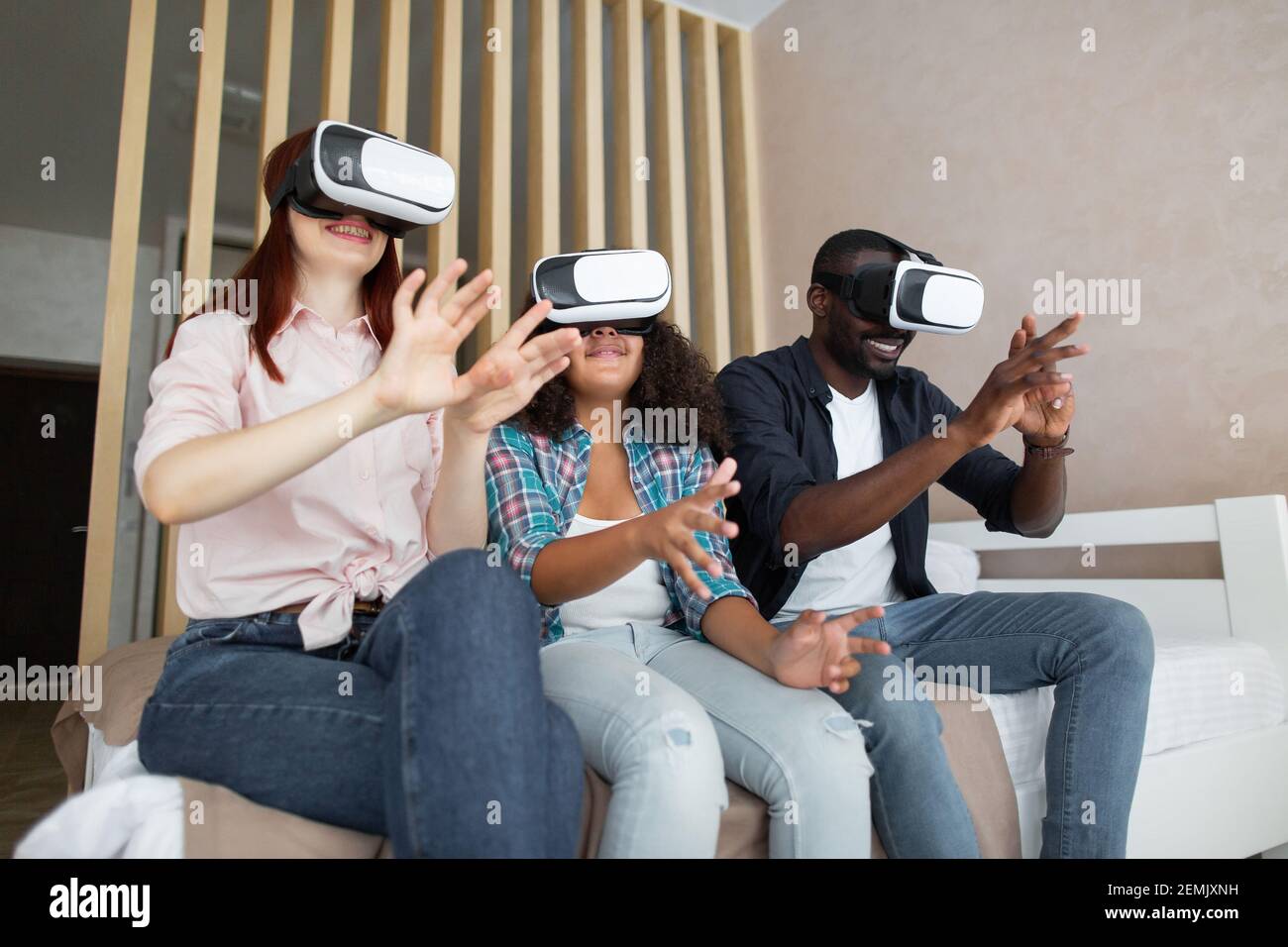 Look at this. Young nice multiethnic family of three wearing virtual reality glasses, gesturing and admiring, while playing video game. New technologi Stock Photo