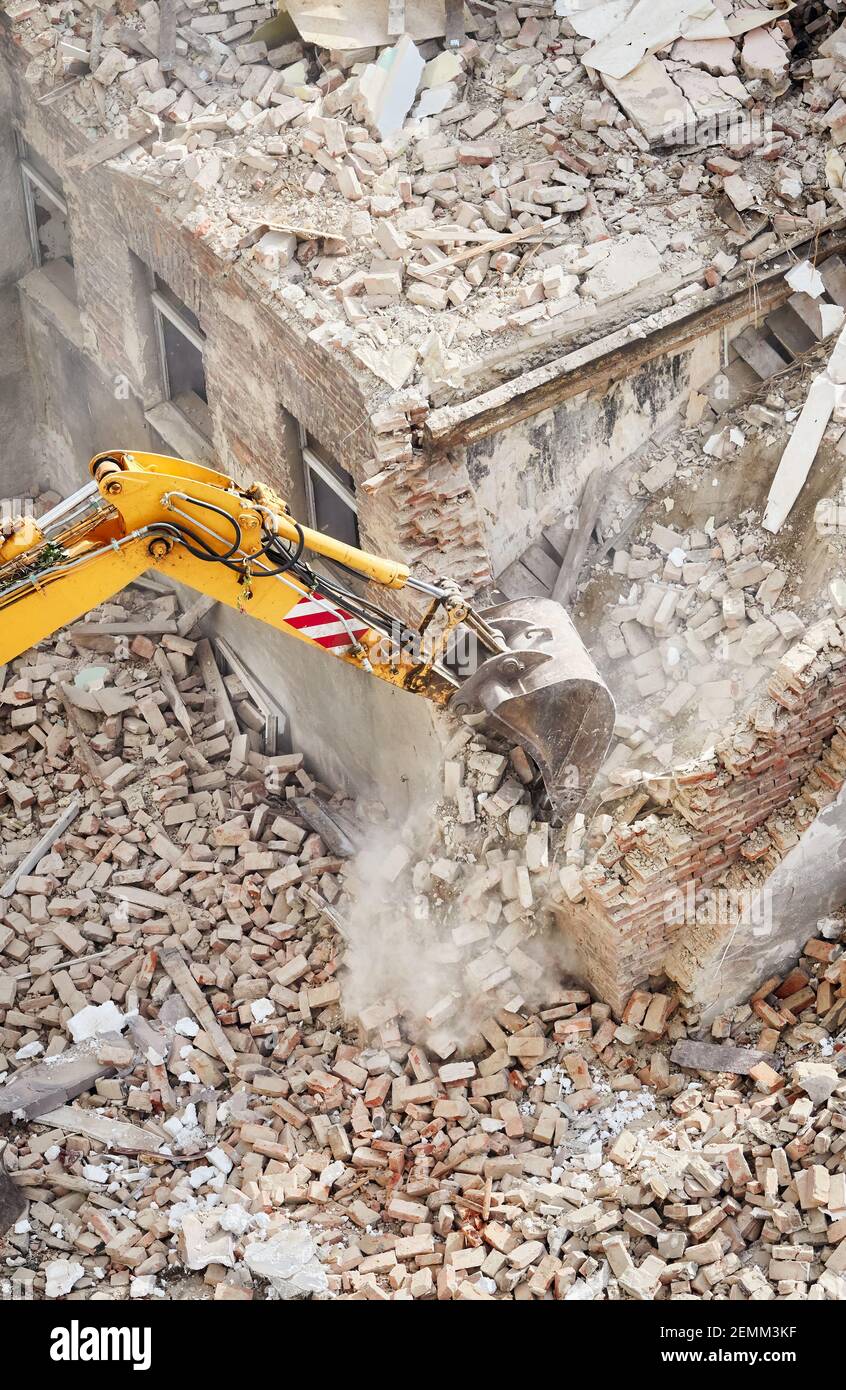 Old brick building demolition with an excavator bucket in dust cloud, view from above. Stock Photo