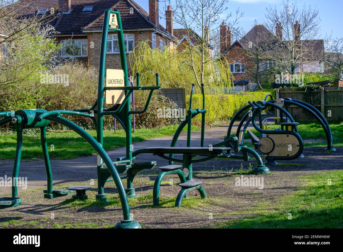 Outside gym equipment surrounded by trees, grass and shrubs with houses
