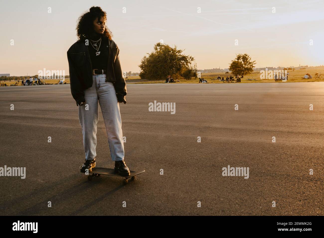 Woman looking away while standing on skateboard in park during sunset Stock Photo