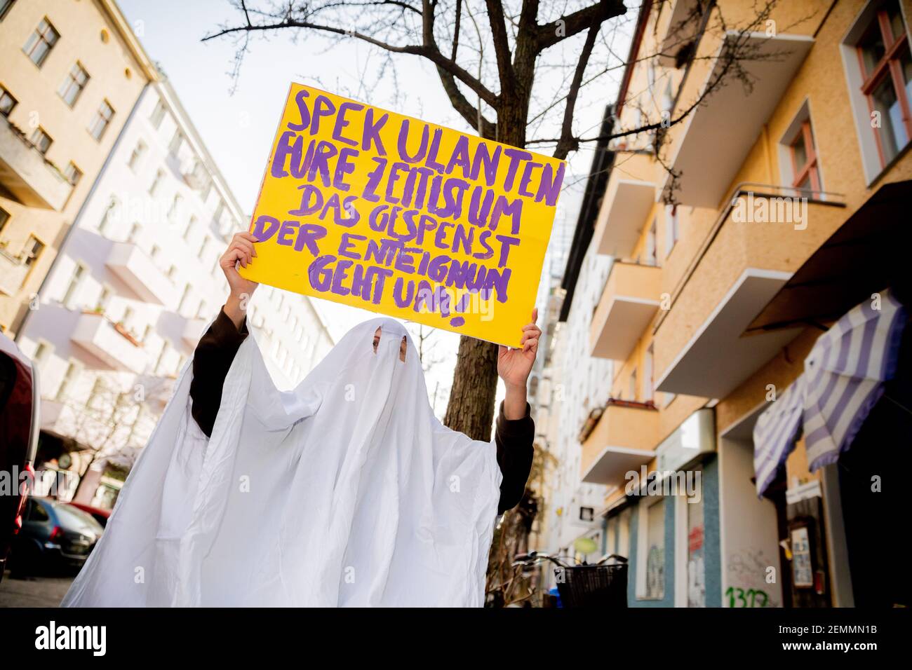 Berlin, Germany. 25th Feb, 2021. An activist in a ghost costume holds a protest sign near the organizing office of the people's petition 'Expropriate Deutsche Wohnen & Co' into the camera. The sign reads 'Spekulanten eure Zeit ist im, das Gespenst der Exteignung geht um!'. On 26.02.2021 begins the second signature phase of the popular initiative to bring about a referendum. The goal is to call on the Berlin Senate to enact a law that regulates the socialization of the apartments of private housing companies, with more than 3000 Berlin apartments. Credit: Christoph Soeder/dpa/Alamy Live News Stock Photo