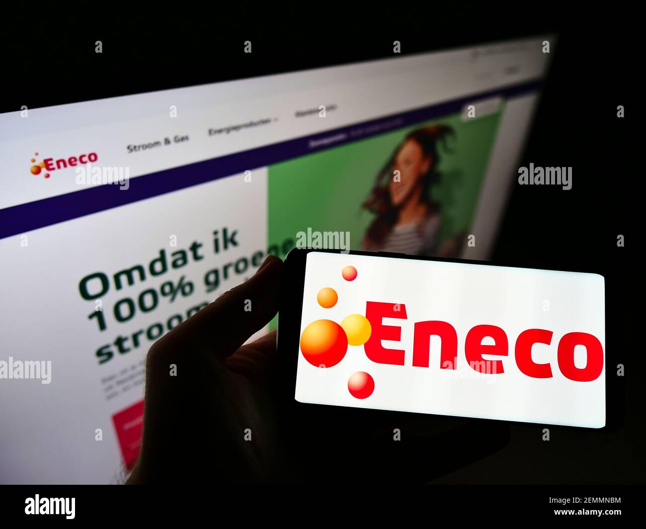 Person holding smartphone with logo of Dutch utility company Eneco Groep N.V. on screen in front of website. Focus on phone display. Unmodified photo. Stock Photo