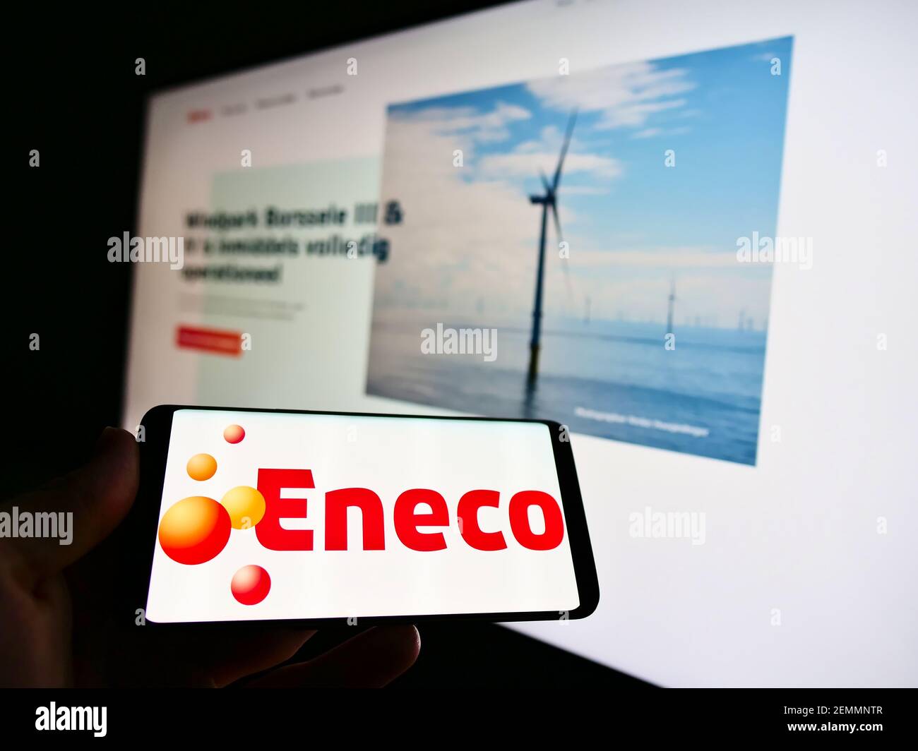 Person holding mobile phone with business logo of Dutch utility company Eneco Groep N.V. on screen in front of web page. Focus on cellphone display. Stock Photo
