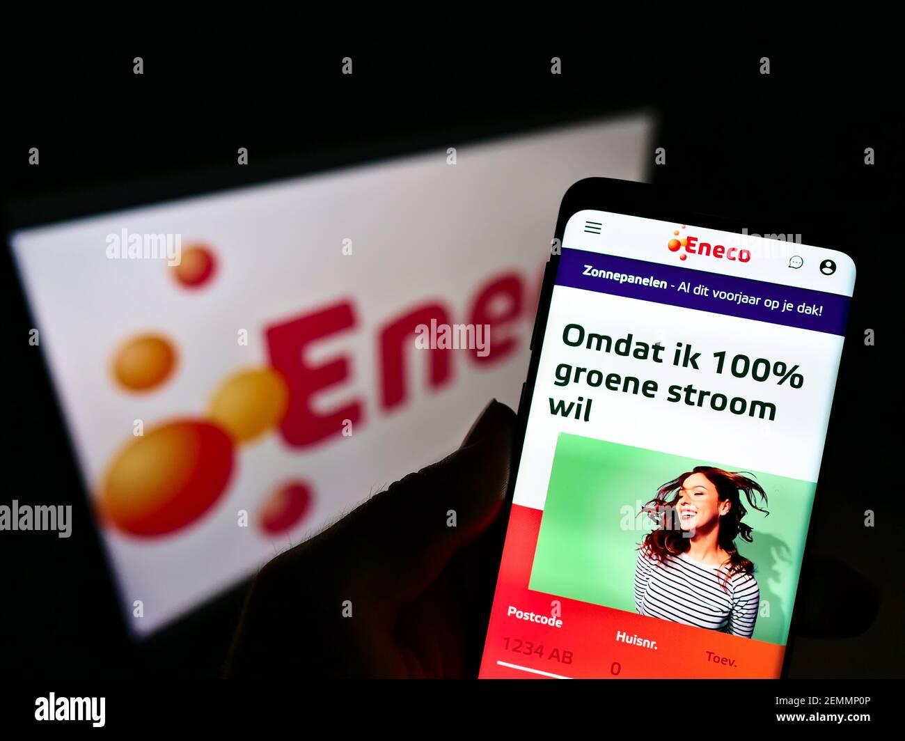 Person holding smartphone with logo of Dutch utility company Eneco Groep NV on screen in front of business website. Focus on center of phone display. Stock Photo