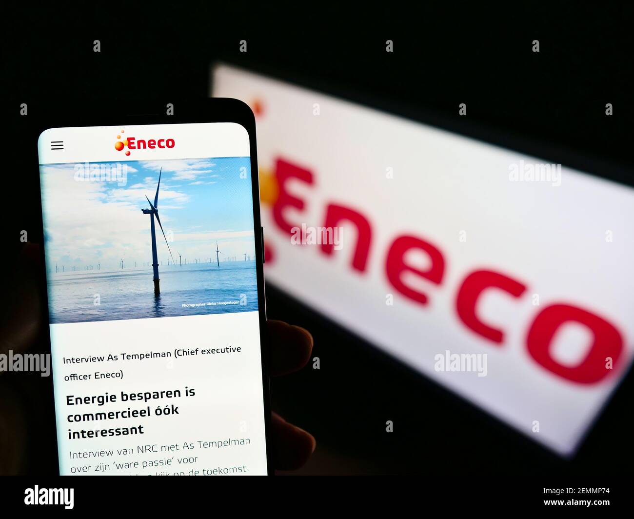 Person holding cellphone with logo of Dutch energy company Eneco Groep N.V. on screen in front of business webpage. Focus on center of phone display. Stock Photo