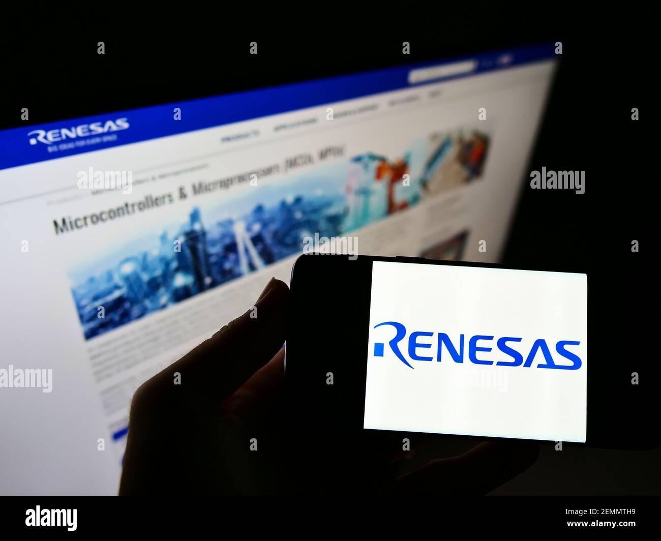 Person holding mobile phone with logo of Japanese company Renesas Electronics Corporation on screen in front of web page. Focus on cellphone display. Stock Photo