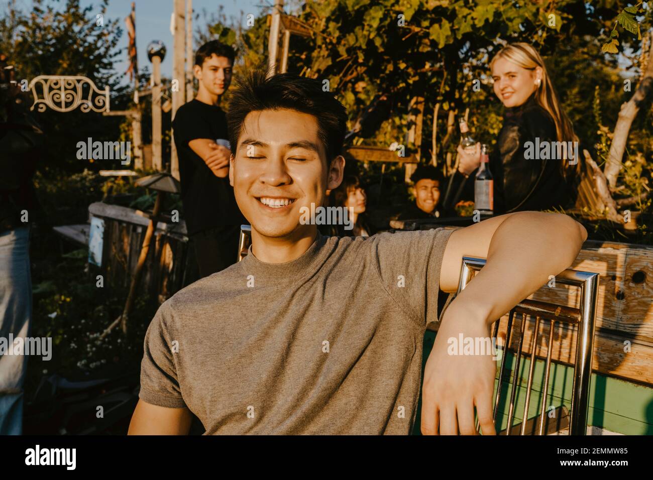 Smiling man sitting on bench while friends in background at park Stock Photo