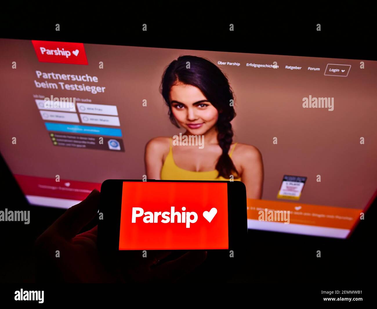 Person holding smartphone with logo of German online dating platform Parship (PE Digital GmbH) on screen in front of website. Focus on phone display. Stock Photo