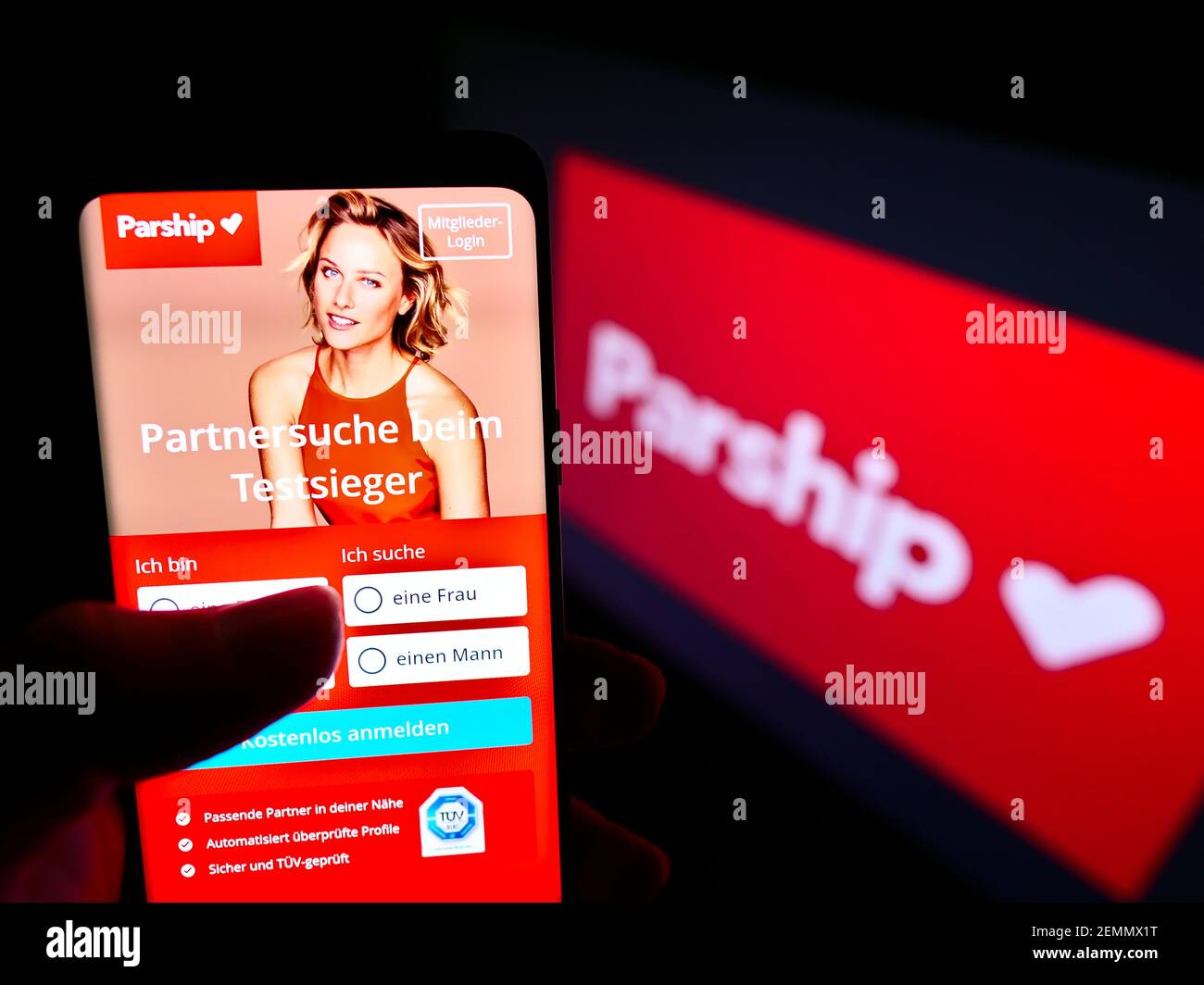 Person holding smartphone with website of German online dating platform Parship on screen in front of company logo. Focus on center of phone display. Stock Photo