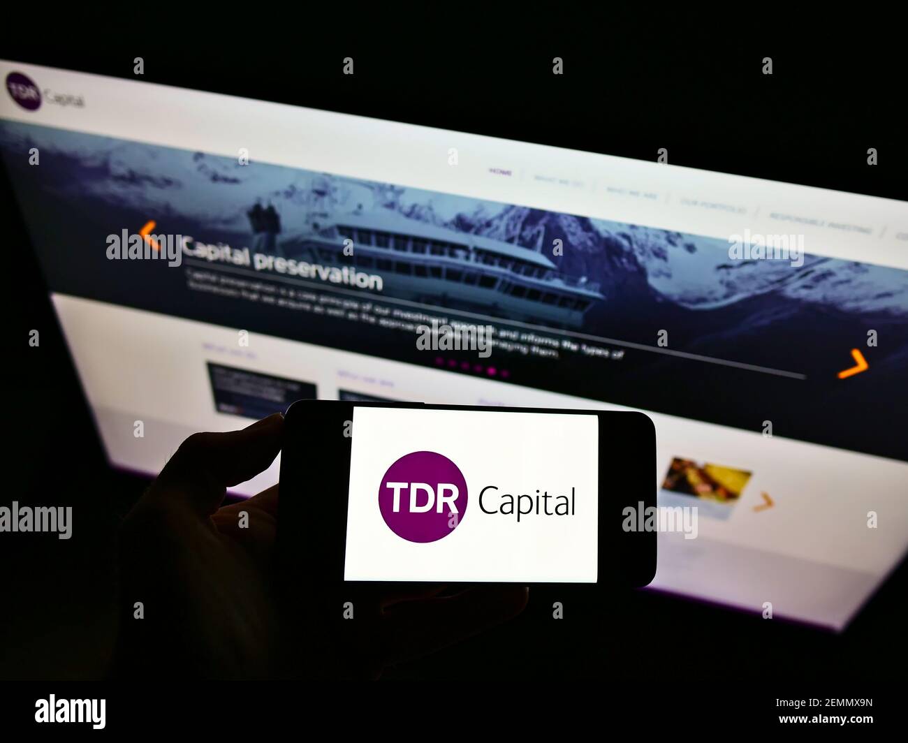 Person holding smartphone with logo of British investment company TDR Capital LLP on screen in front of website. Focus on phone display. Stock Photo