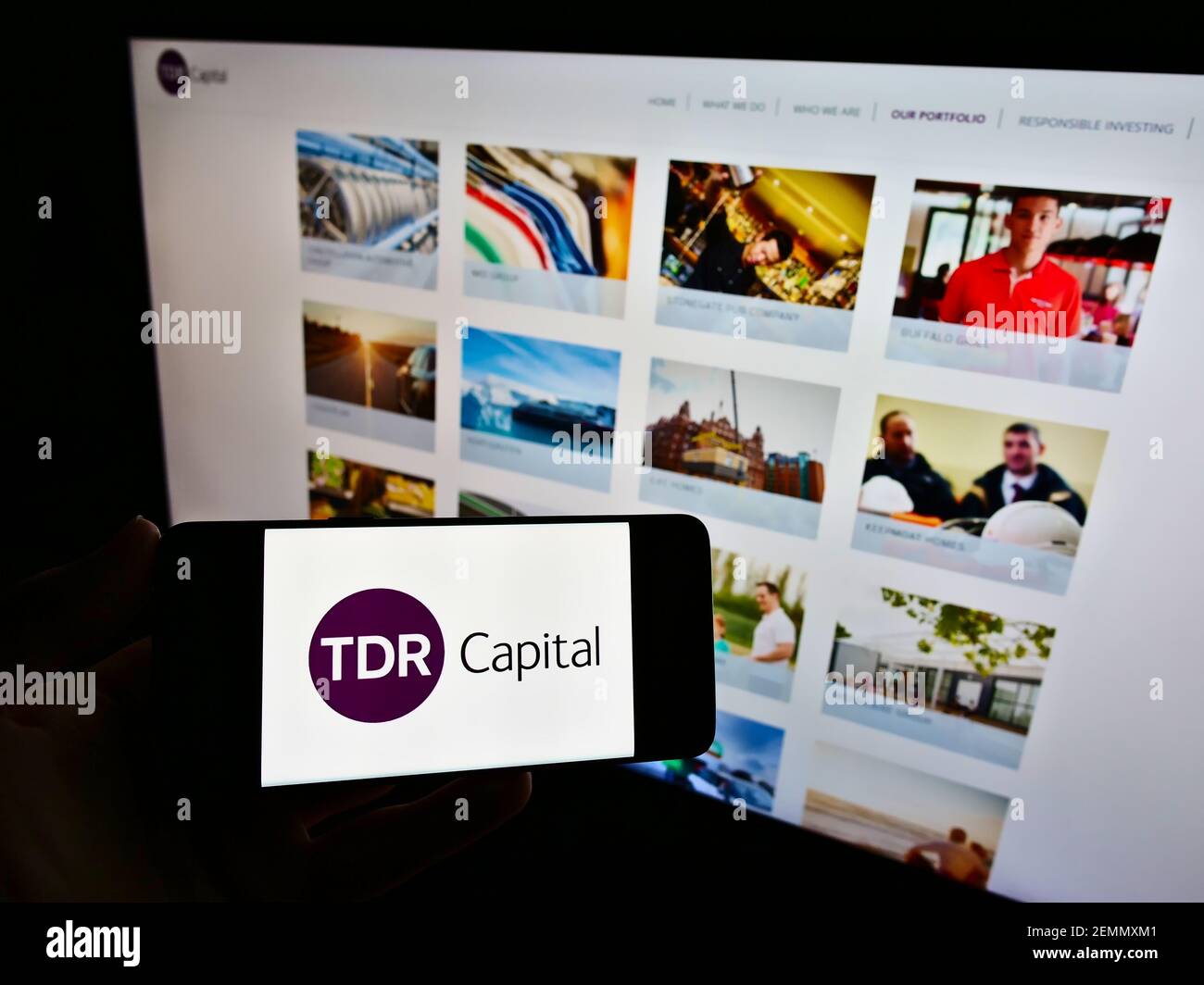 Person holding mobile phone with business logo of British investment company TDR Capital LLP on screen in front of website. Focus on phone display. Stock Photo