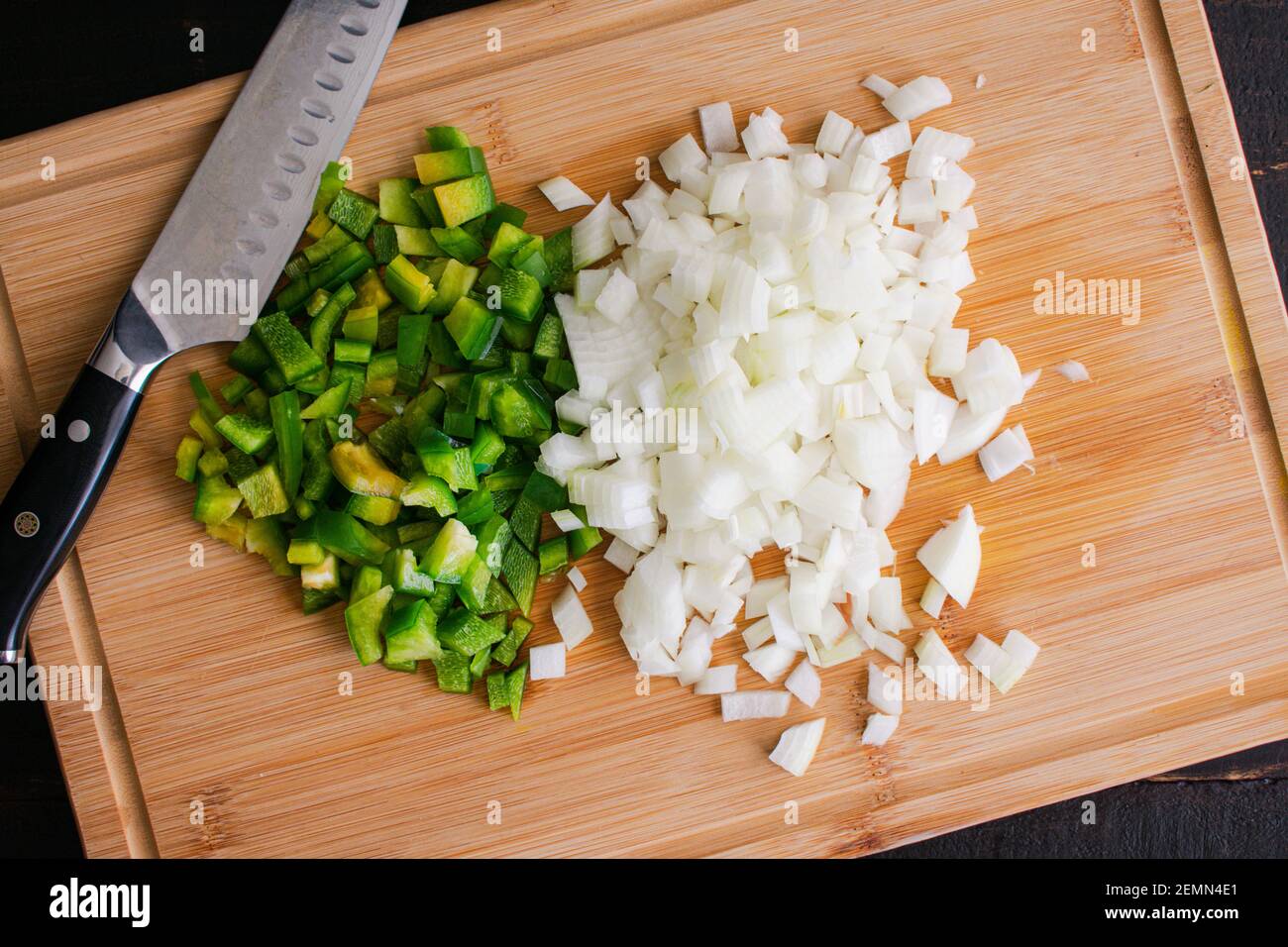 Chopped Green Bell Pepper and Onion on a Bamboo Cutting Board: Overhead view of diced vegetables on a wooden chopping board Stock Photo