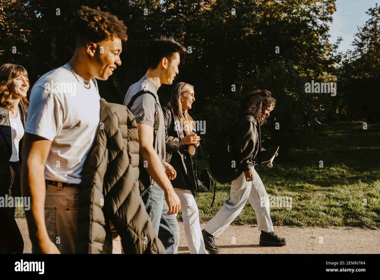 Happy male and female friends walking on road in park Stock Photo