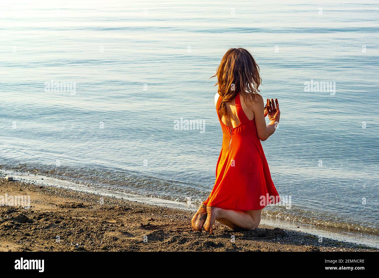 woman in red dress kneeling by the sea Stock Photo Alamy