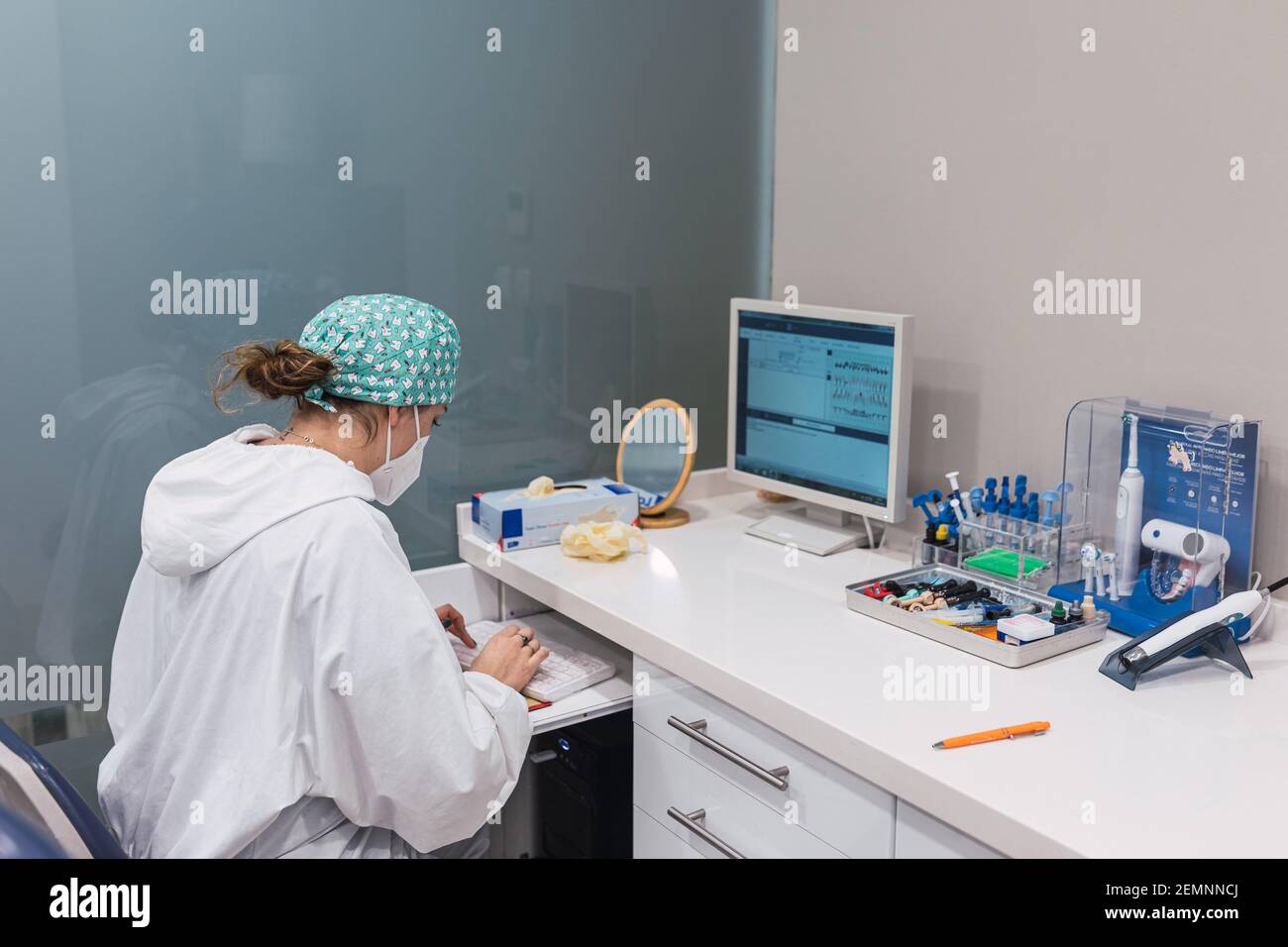 Female dentist using computer at office desk. Looking at the screen