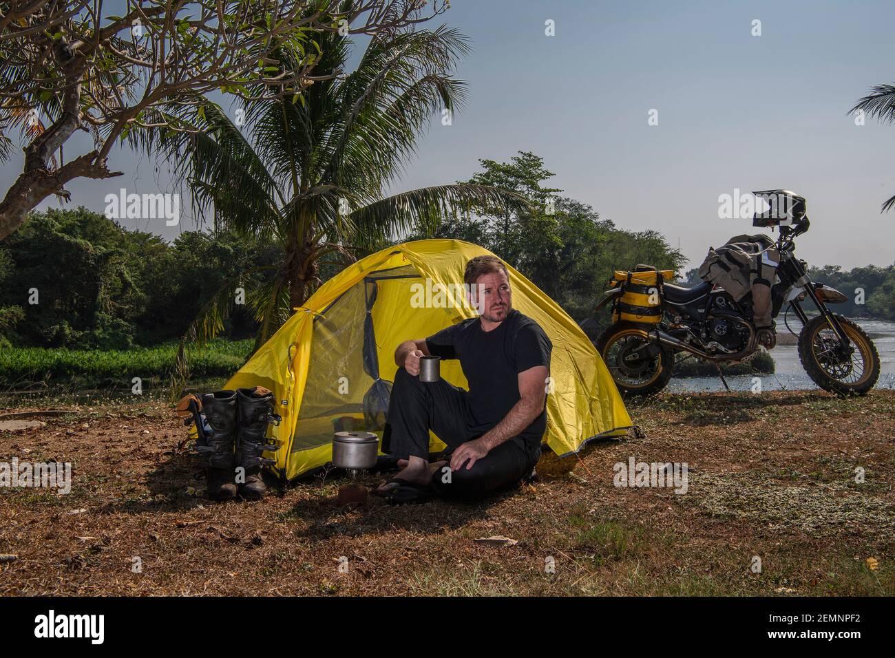 man camping next to river Kwai with his off road motorcycle Stock Photo