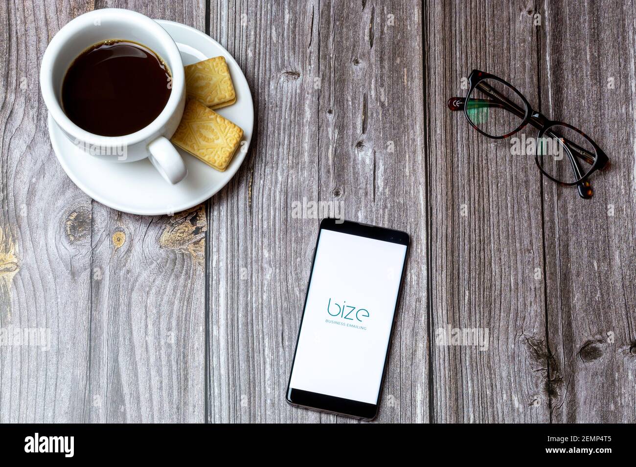 A mobile phone or cell phone on a wooden table with the Bize Business Emailing app open next to a coffee Stock Photo