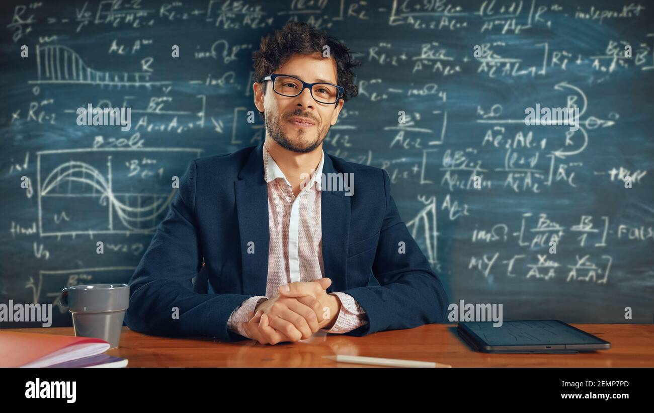Online e-Education: Teacher Sitting at Desk, Explains Lesson to a Classroom, Behind Him Blackboard with Writing. e-Learning, Online Courses: Lecturer Stock Photo