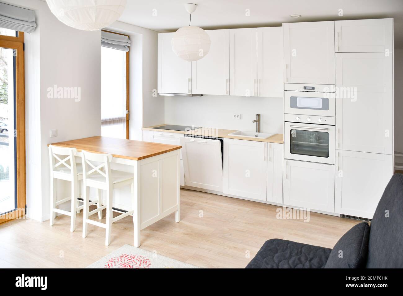 Modern Scandinavian-Style kitchen or living room, minimalist interior design, oven, microwaves and sink with wooden board, table and chairs, white Stock Photo