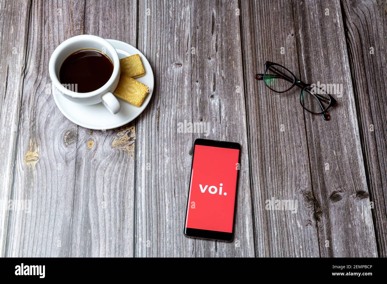 A mobile phone or cell phone on a wooden table with the VOI scooters app open next to a coffee and glasses Stock Photo