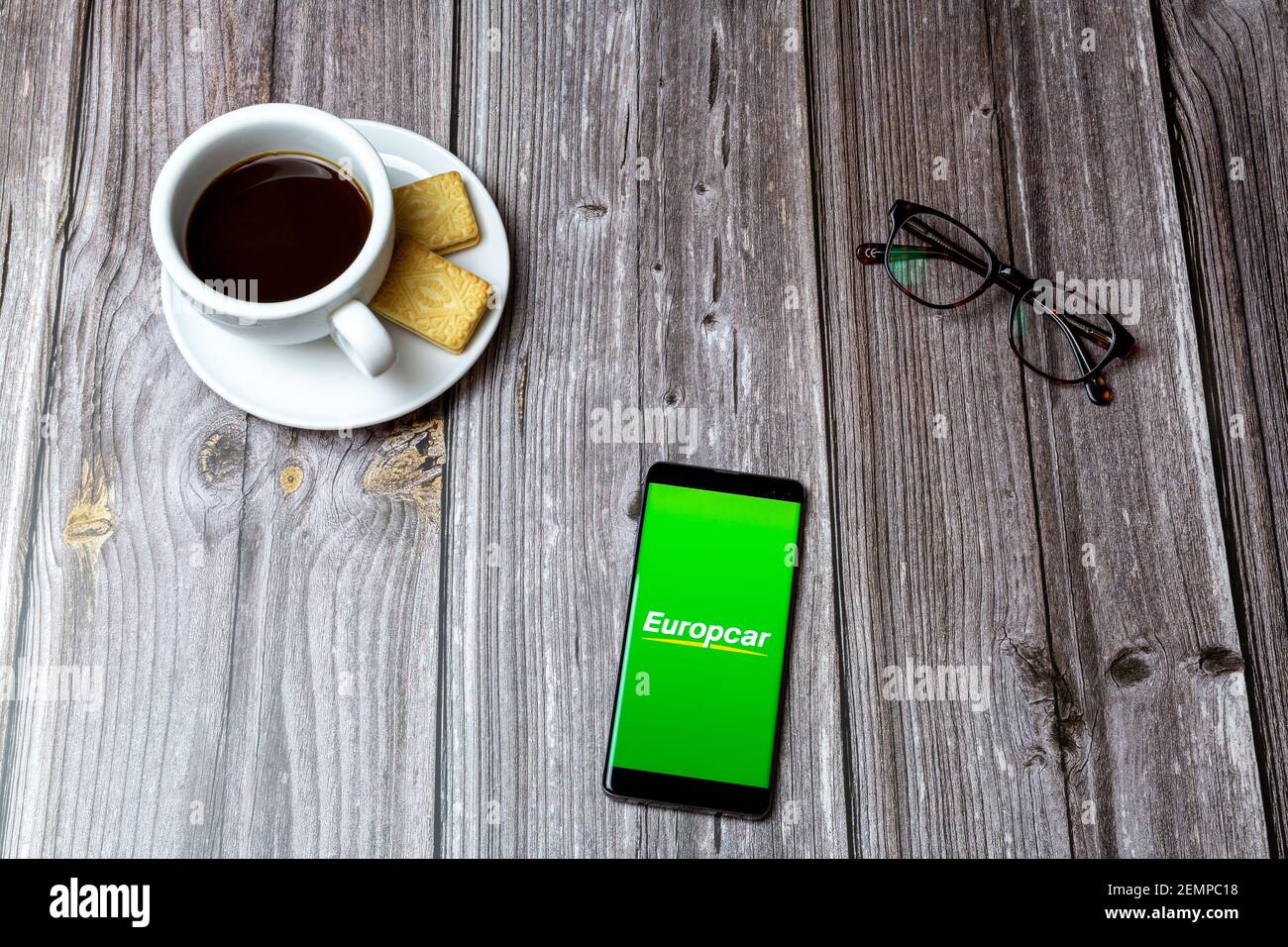 A mobile phone or cell phone on a wooden table with the Europcar app open next to a coffee and glasses Stock Photo
