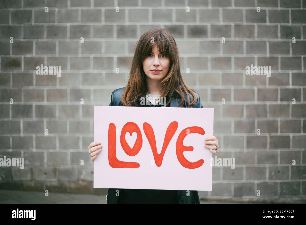 Portrait of female activist with love poster against wall Stock Photo