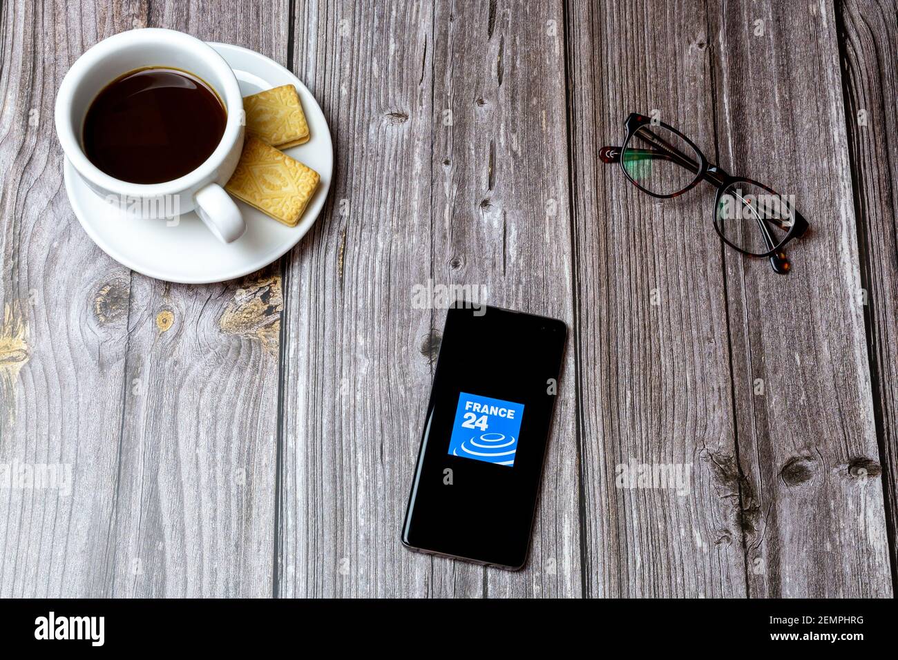 A mobile phone or cell phone on a wooden table with the France 24 news app open next to a coffee and glasses Stock Photo