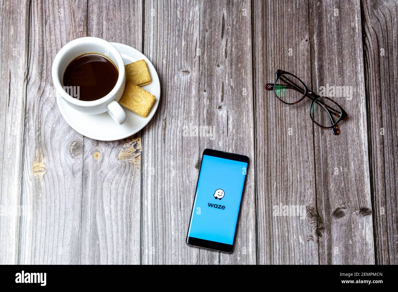 A mobile phone or cell phone on a wooden table with the Waze Maps app open next to a coffee and glasses Stock Photo