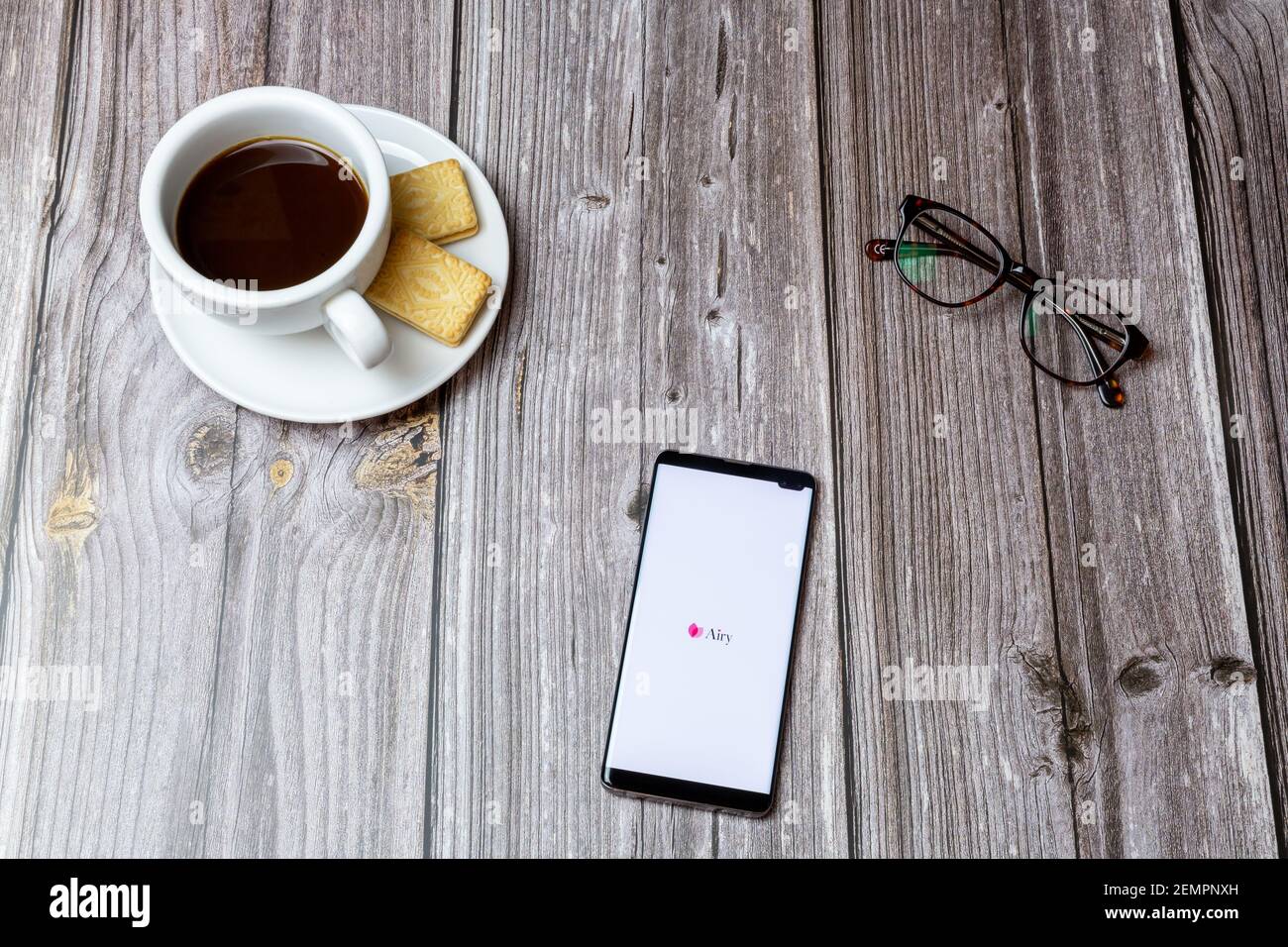 A mobile phone or cell phone on a wooden table with the Airy app open next to a coffee and glasses Stock Photo