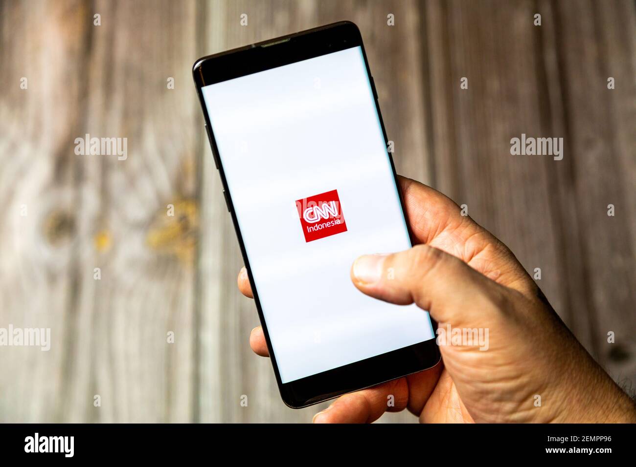 A mobile phone or cell phone being held by a hand with the CNN Indonesia app open on screen Stock Photo