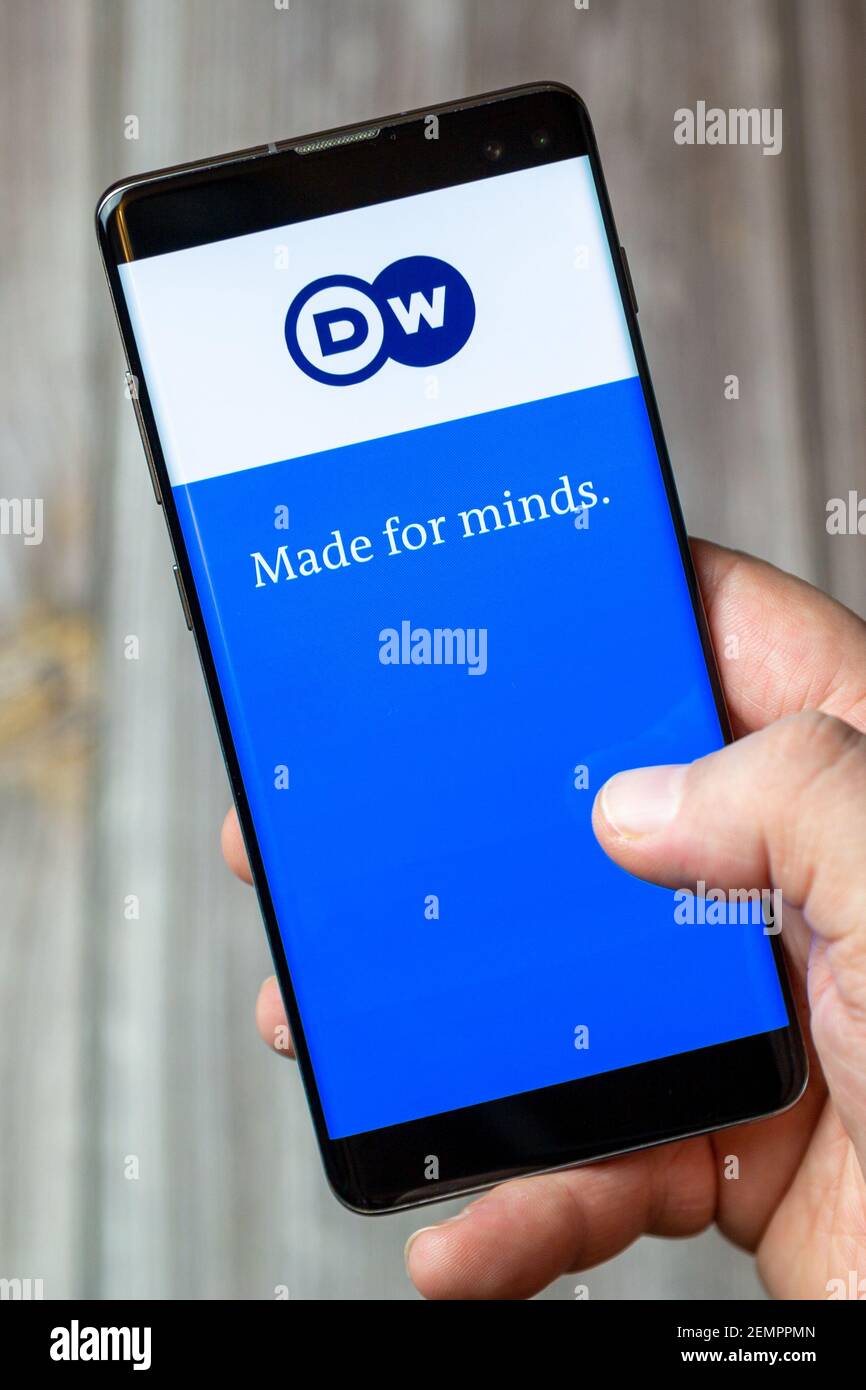 A mobile phone or cell phone being held by a hand with the Deutsche Welle app open on screen Stock Photo