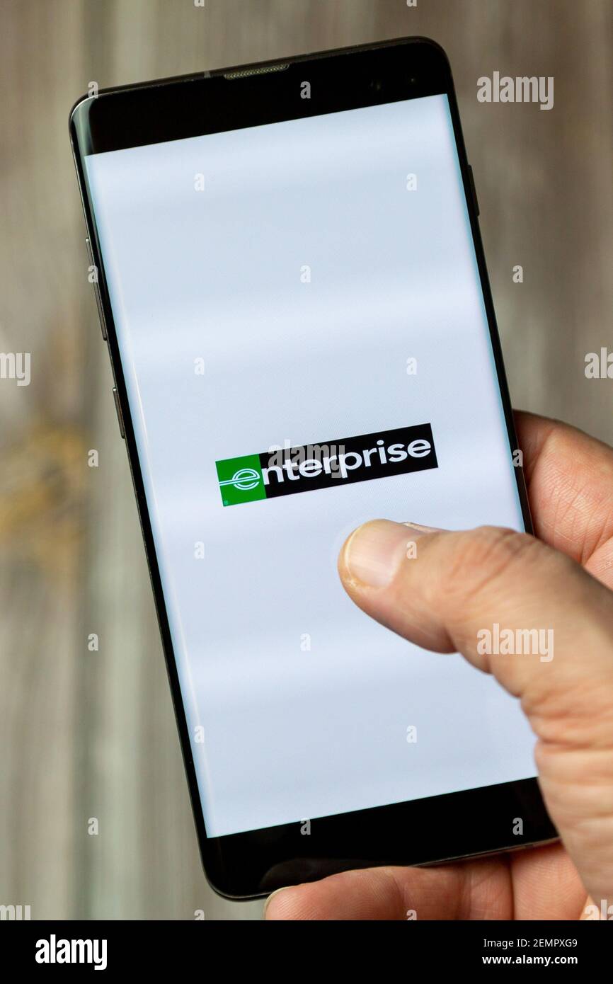 A mobile phone or cell phone being held by a hand with the Enterprise car hire app open on screen Stock Photo