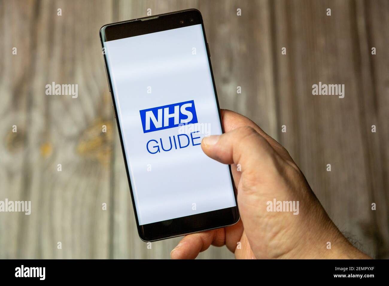 A mobile phone or cell phone being held by a hand with the NHS Guide app open on screen Stock Photo