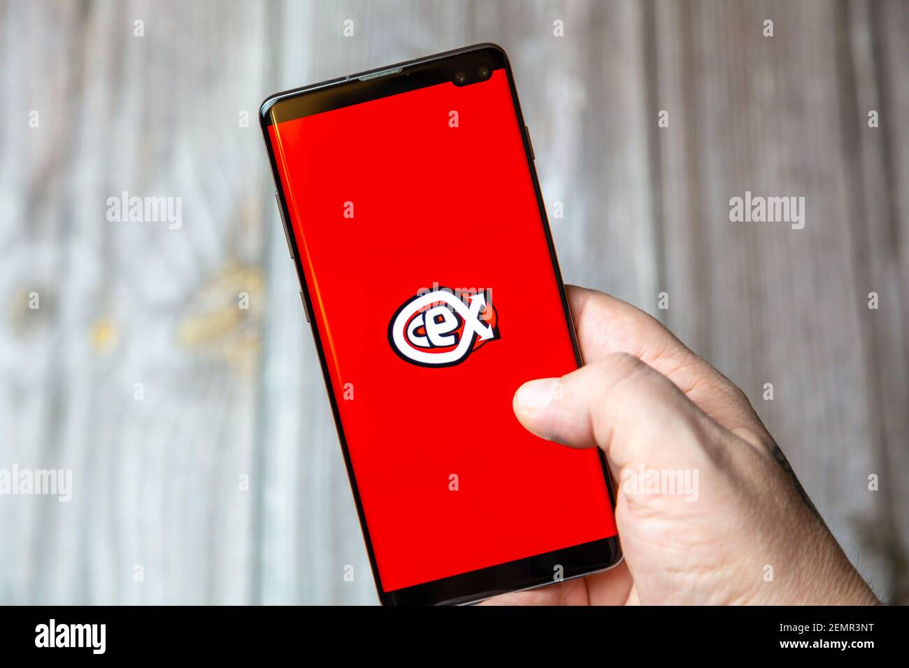 A mobile phone or cell phone being held by a hand with the CEX app open on screen Stock Photo